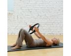 Femme allongée sur un tapis de gym avec un Pilates Circle 36 cm Femme allongée sur un tapis de gym avec un Pilates Circle 36 cm
