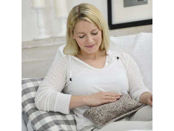 Femme utilisant la bouillotte électrique SISSEL® Heat Wave taupe sur son ventre Femme utilisant la bouillotte électrique SISSEL® Heat Wave taupe sur son ventre