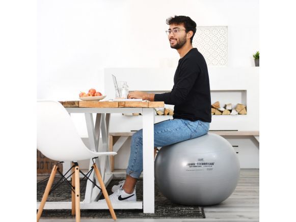 Homme assis sur le ballon de Gymnastique SISSEL® SECUREMAX® Ø65 cm en télétravail Homme assis sur le ballon de Gymnastique SISSEL® SECUREMAX® Ø65 cm en télétravail