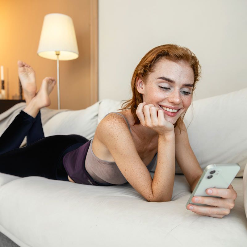 Femme utilisant la ceinture chauffante lombaire Vulpés prune sur son lit Femme utilisant la ceinture chauffante lombaire Vulpés prune sur son lit